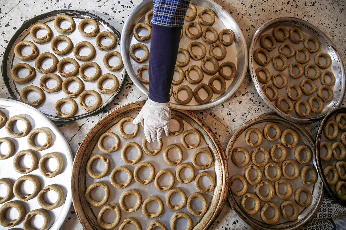 A Palestinian woman, wearing protective face masks and gloves during the COVID-19 pandemic, checks on formed traditional cookies in preparation for the upcoming Eid al-Fitr holiday which marks the end of the Islamic holy month of Ramadan, in the southern Gaza Strip city of Rafah on May 17, 2020. (Photo by AFP)