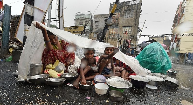 A family sits under a polythene sheet during rain in Kolkata. PTI