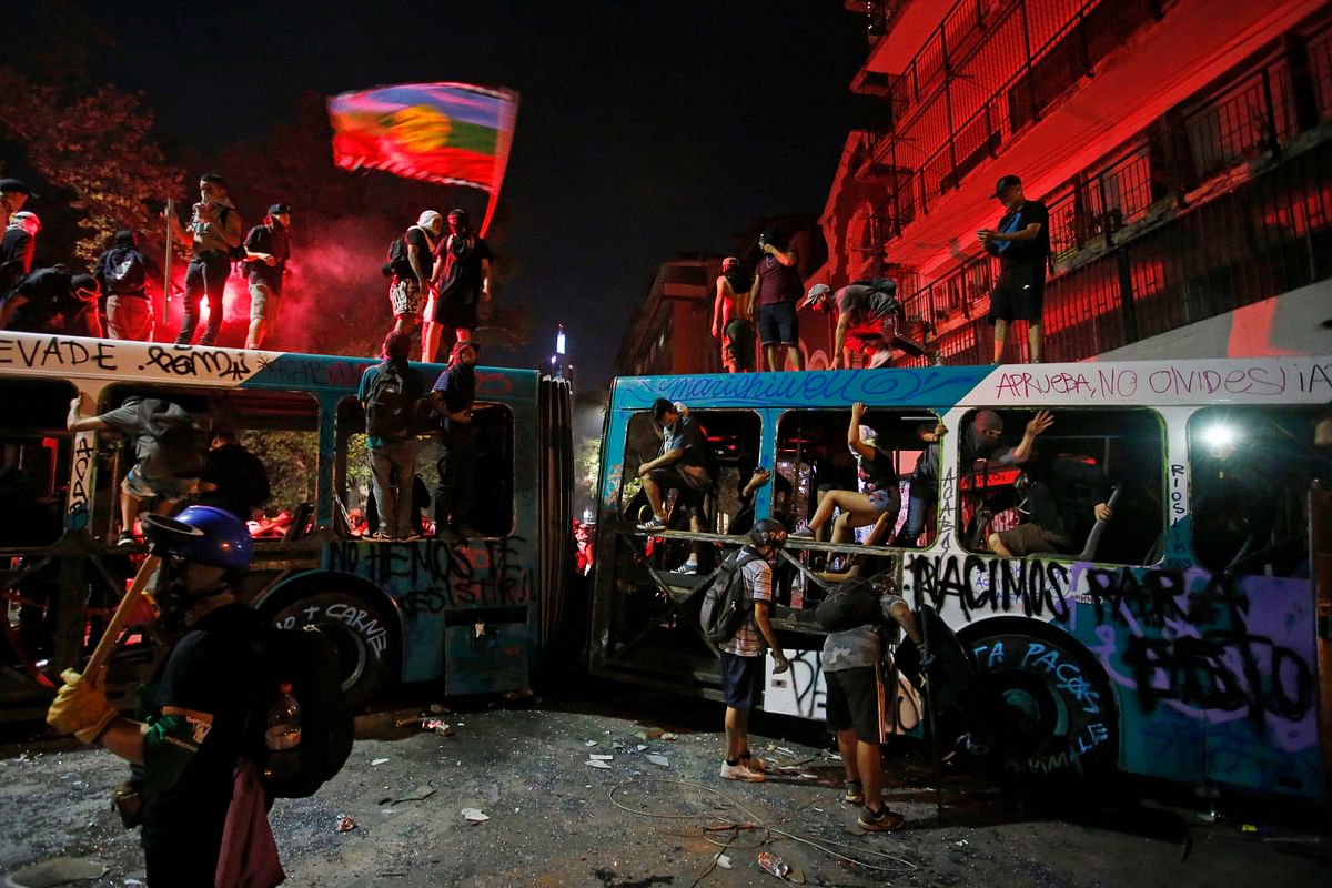 Demonstrators stand on a destroyed a bus during an anti-government protest in Santiago, Chile. (Credit: AP)