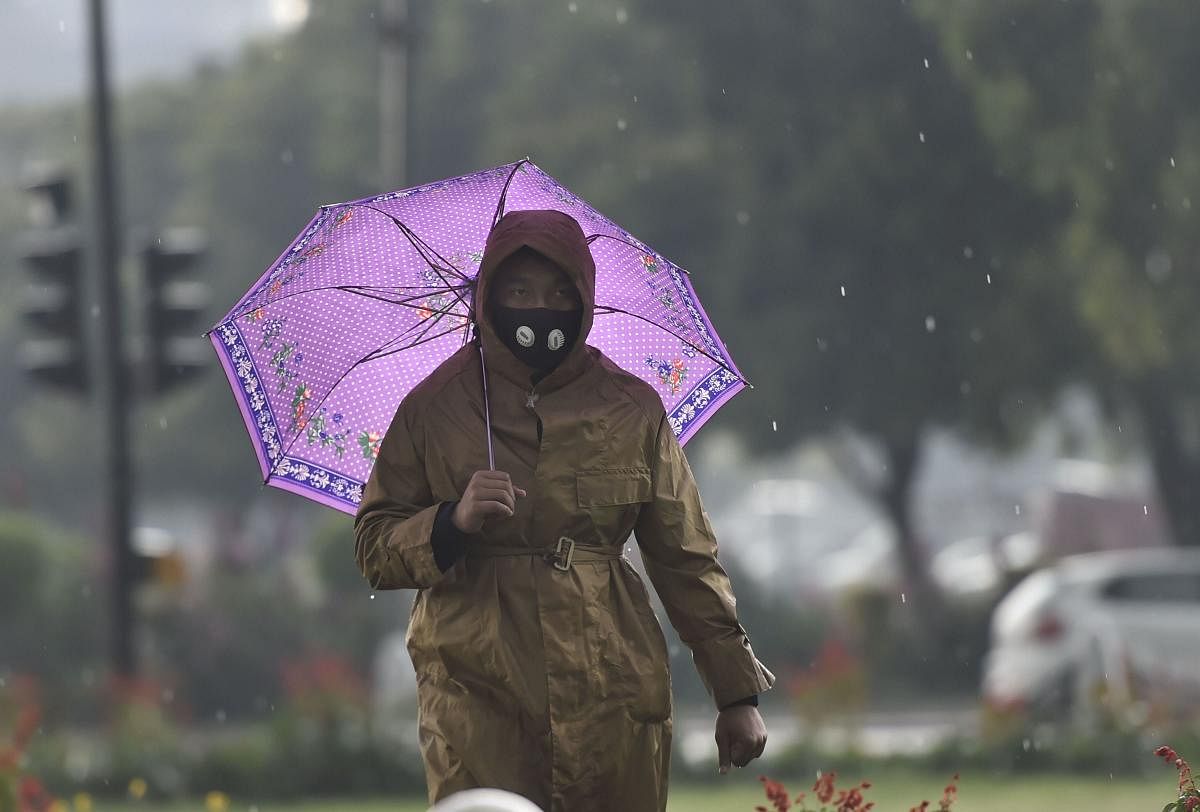 A man wearing protective mask in view of novel coronavirus pandemic holds an umbrella as heavy rains accompanied by hailstorm lashed parts of the national capital, at Rajpath in New Delhi, Saturday, March 14, 2020. (PTI Photo/Ravi Choudhary)