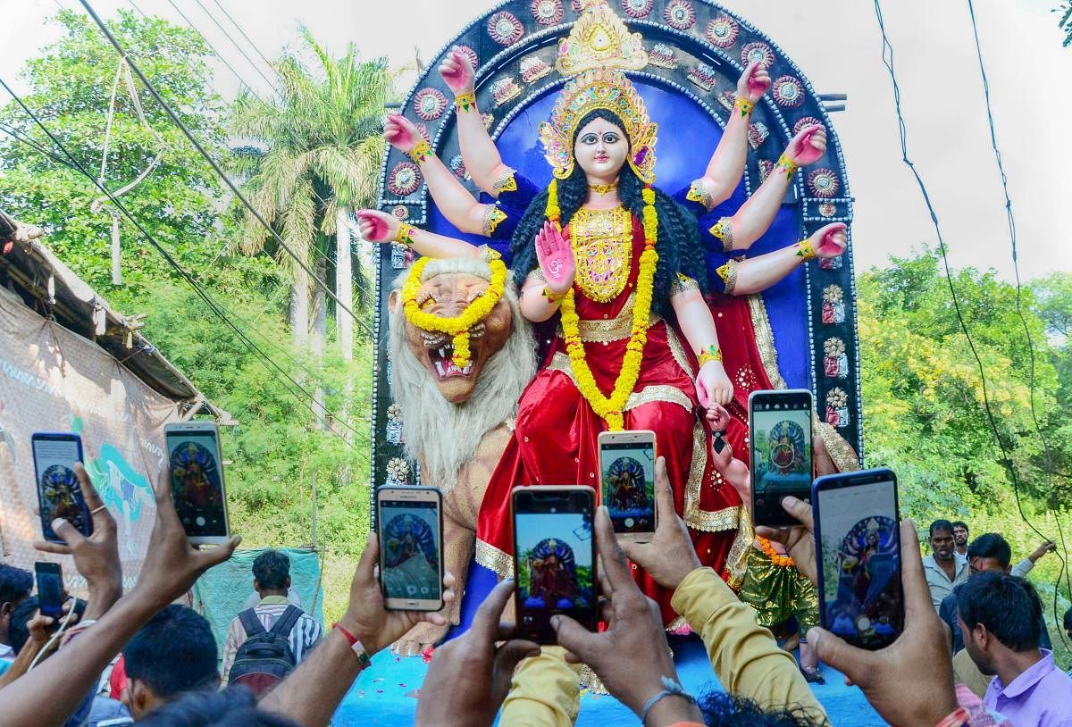Devotees carry an idol of Goddess Durga for installation at a puja pandal as ther take photos on their mobile phones, on the eve of Navratri festival, in Bhopal. (PTI photo)