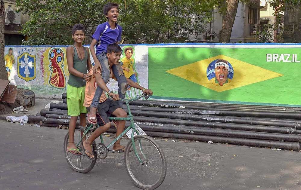 Boys ride a cyle as they move past a wall painted with the pictures of Brazilian footballers, in Kolkata on Sunday, June 03, 2018, ahead of FIFA World Cup 2018. PTI Photo
