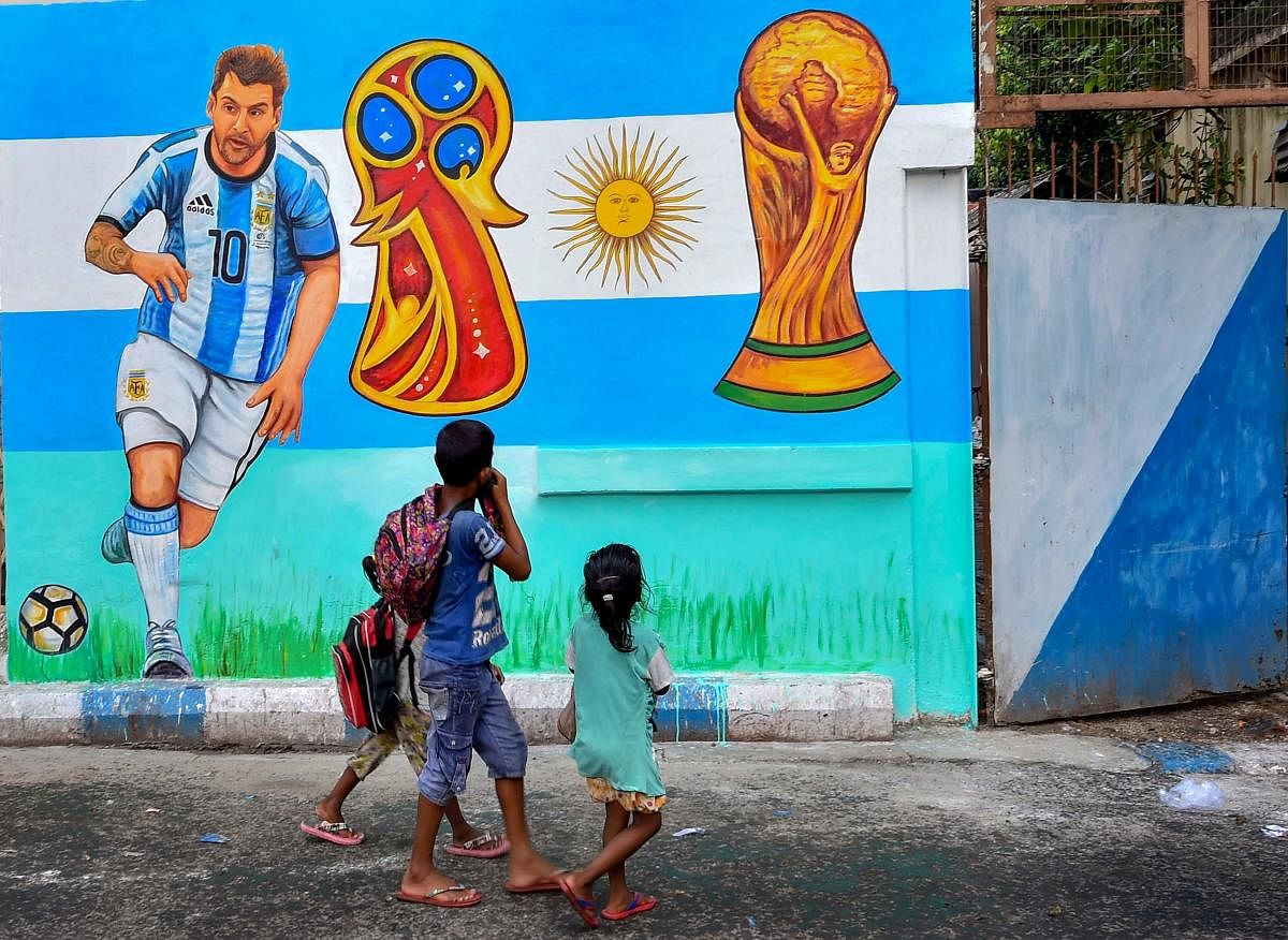 Children walk past a wall graffiti of Argentine footballer Lionel Messi as FIFA fever grips various parts of the country, in Kolkata on Thursday. PTI Photo