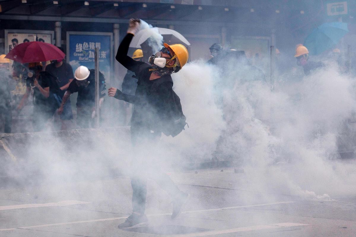 A protester throws back tear gas fired by the police in Wong Tai Sin during a general strike in Hong Kong (AFP Photo)