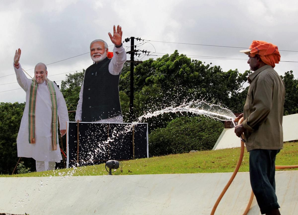 A worker sprinkles water with the cutouts of Prime Minister Narendra Modi and BJP President Amit Shah in the backdrop, ahead of BJP's public meeting, in Bhubaneswar, on Friday. PTI Photo