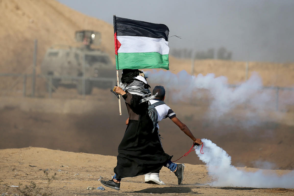 A woman holding a Palestinian flag runs as tear gas fired by Israeli forces during an-anti Israel protest, at the Israel-Gaza border fence in the southern Gaza Strip on August 23, 2019. (REUTERS/Ibraheem Abu Mustafa)