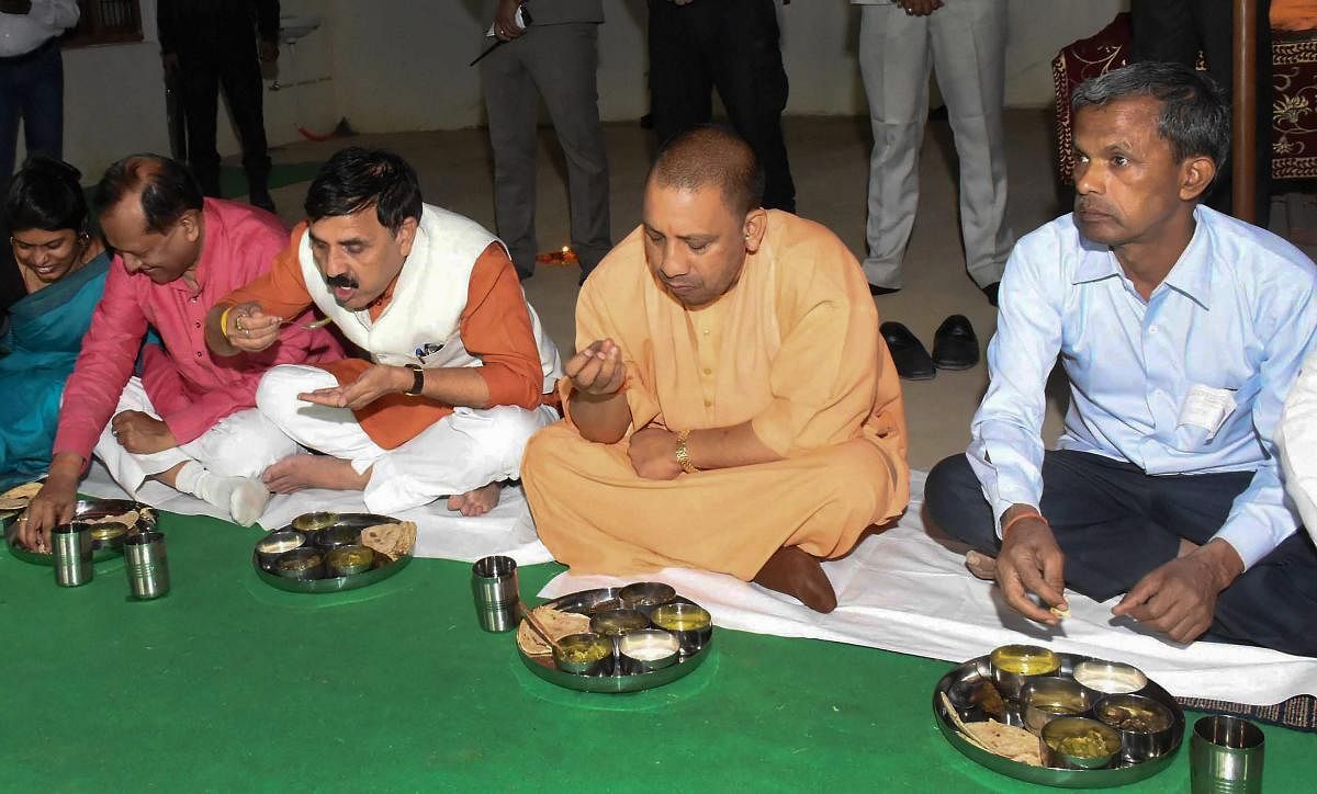 Uttar Pradesh Chief Minister Yogi Adityanath with MP Vinod Kumar Sonkar eat dinner at a Dalit family's home during their visit to Kandhaipur Madhupur village in Pratapgarh district on late Monday. PTI Photo