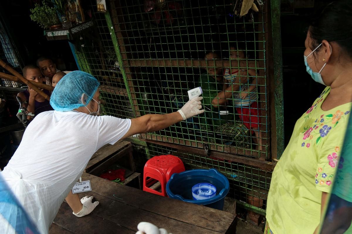 A volunteer wearing protective gear amid concerns over the spread of the COVID-19 coronavirus takes the temperature of a resident while going door-to-door for health check-ups in Yangon on May 17, 2020. Credit: AFP Photo