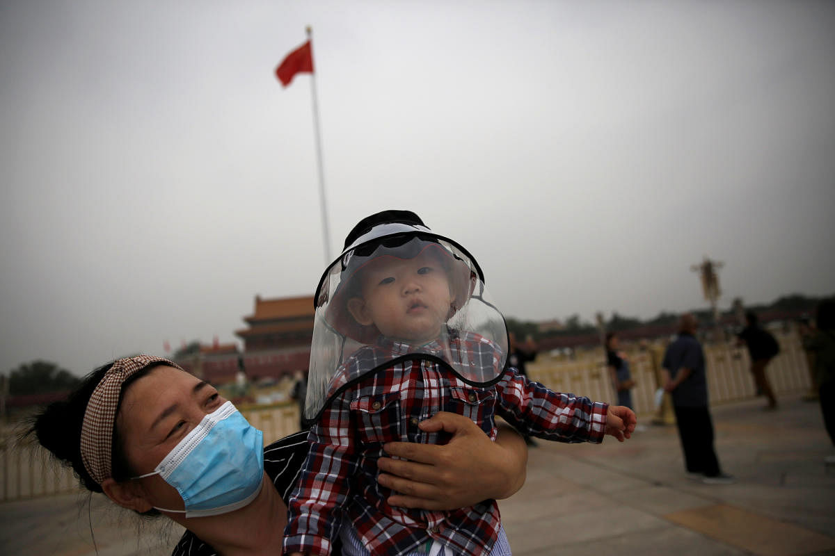 Woman holds a child who wears a protective face cover as they pose for pictures near a Chinese national flag at the Tiananmen Square in Beijing. Credit: Reuters Photo