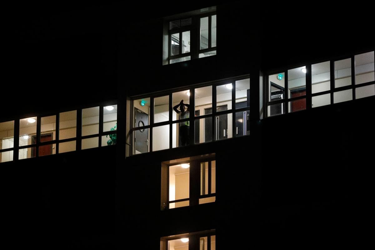 A resident looks out the window of an apartment building as French CRS anti-riot police officers walk below during clashes in Villeneuve-la-Garenne, in the northern suburbs of Paris, late on April 21, 2020.  Credit: AFP Photo