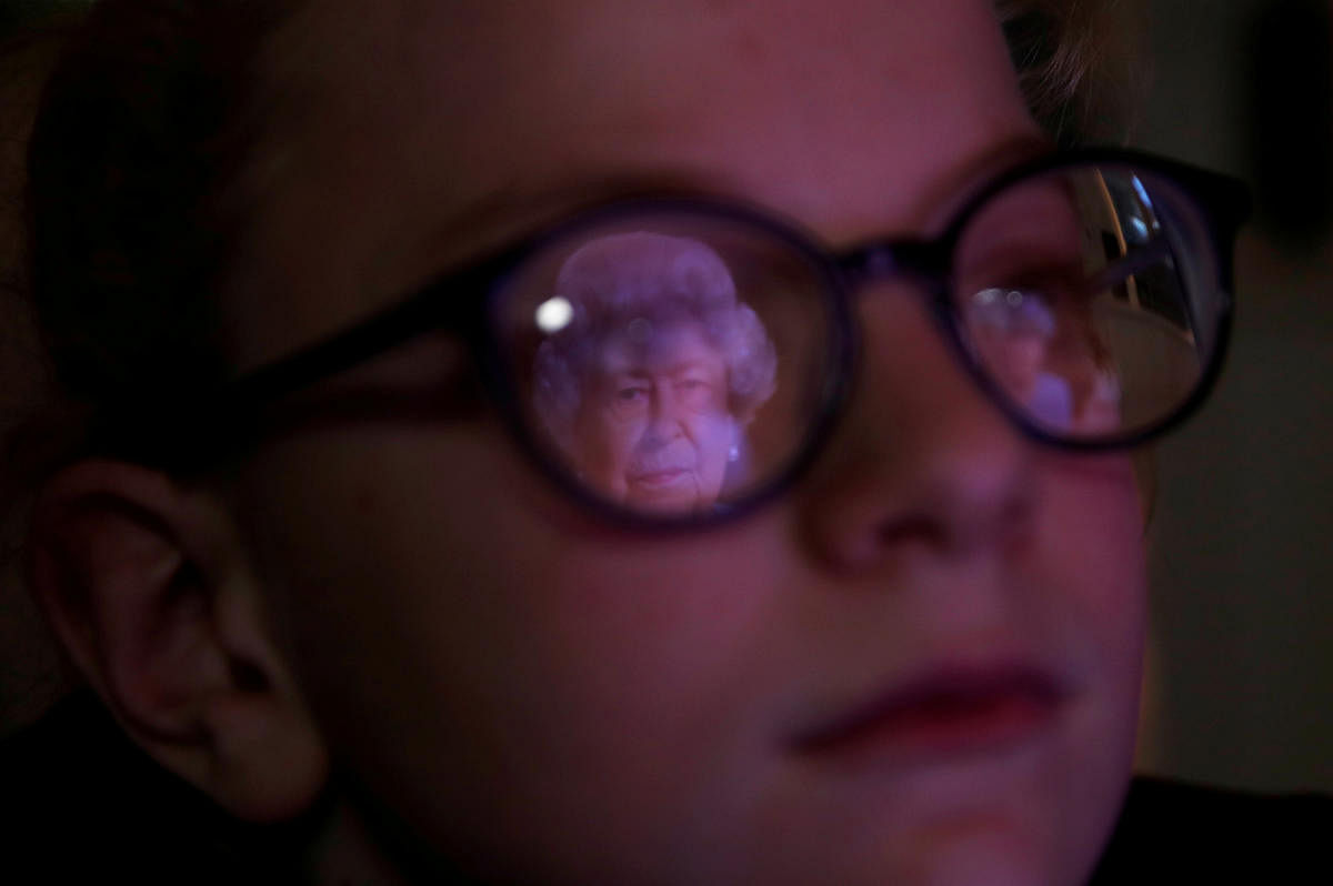 Lucy at her home in Manchester looks on as Britain's Queen Elizabeth II is reflected in her glasses during her address to the nation and the Commonwealth on the 75th anniversary of VE Day, Manchester, Britain, May 8, 2020. Credit: Reuters Photo