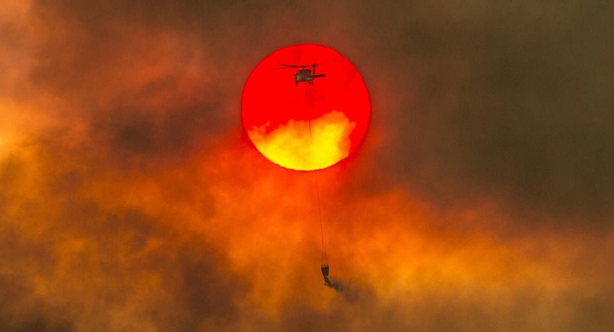 Redding : In this Friday, July 27, 2018 photo, a firefighting helicopter makes a water drop as the sun sets over a ridge burning near Redding, Calif., in efforts against the Carr Fire. Scorching heat, winds and dry conditions complicated firefighting efforts. AP/ PTI