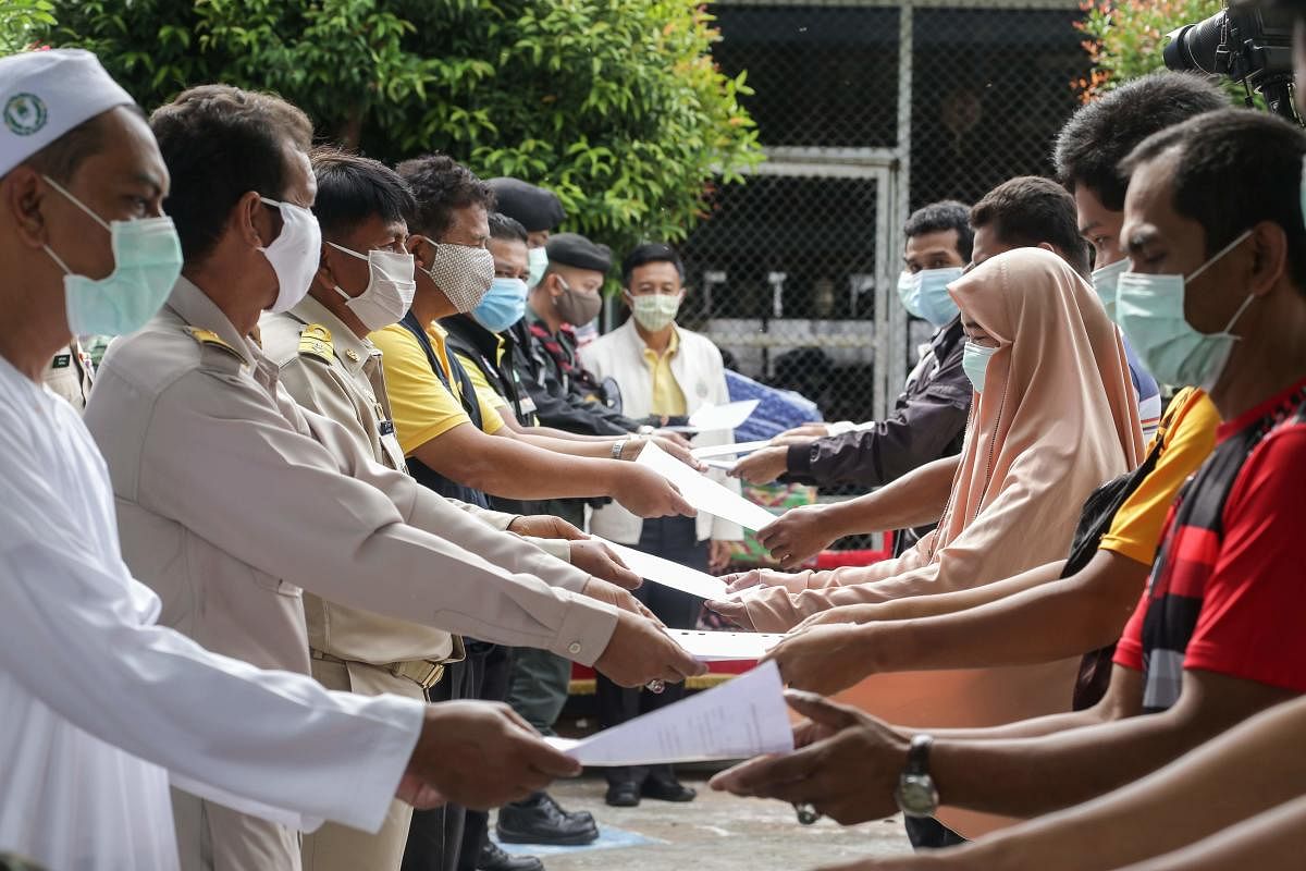 Thai officials (L) pose as they hand over certificates to people allowed to leave a 14-day quarantine imposed to halt the spread of the COVID-19 coronavirus at a school in Panaret, in southern Thailand's Pattani province on May 17, 2020. Credit: AFP Photo