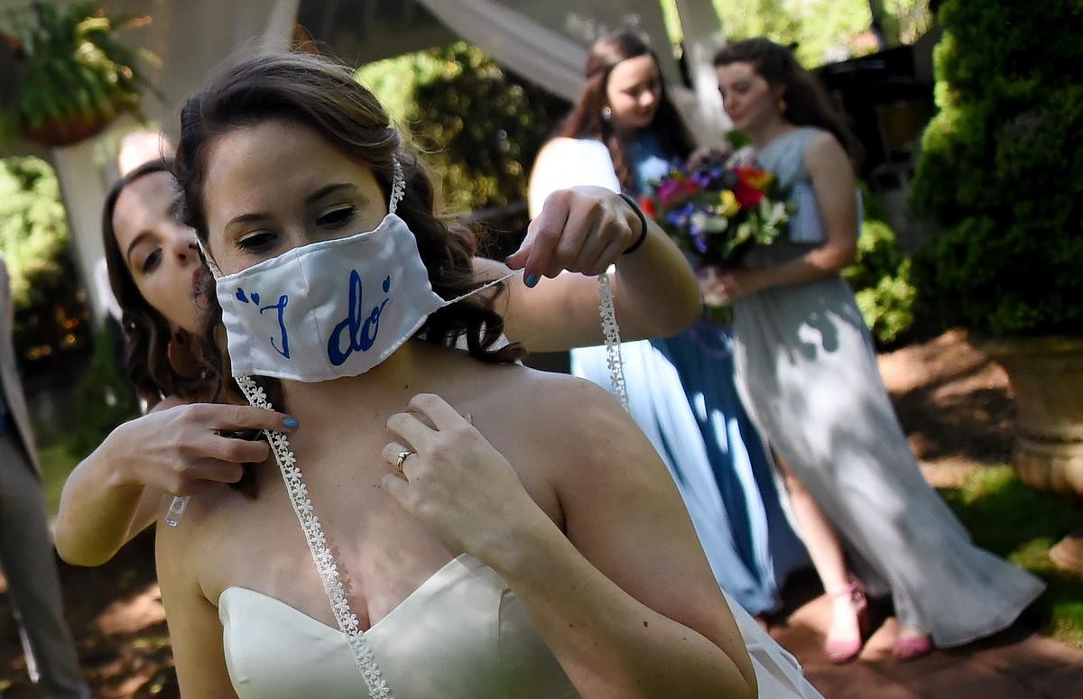 A bridesmaid assists bride Rachel Vasquez with her face mask following her wedding ceremony on May 9, 2020 at the Glencliff Manor in Rustburg, Virginia. Credit: AFP Photo