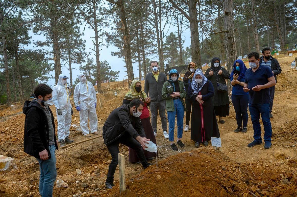Relatives pray for a relative who died of COVID-19, as morgue workers, wearing a protective suit and a face mask, stand next to them, at a cemetery in Istanbul. (AFP Photo)