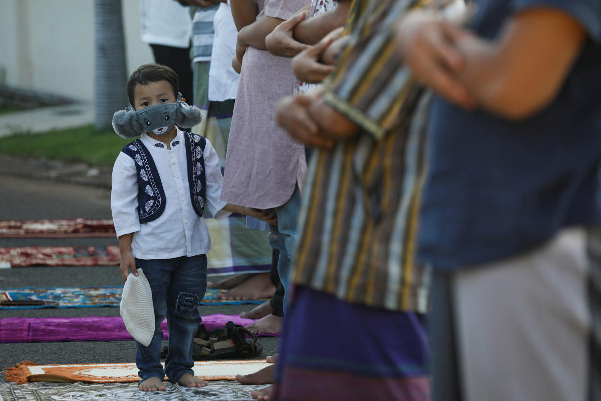 A kid wearing protective mask looks on as people pray to celebrate Eid al-Fitr, the Muslim festival marking the end the holy fasting month of Ramadan, at a residential area amid the spread of coronavirus disease (COVID-19) outbreak in Bekasi, on the outskirts of Jakarta, Indonesia. (Reuters photo)