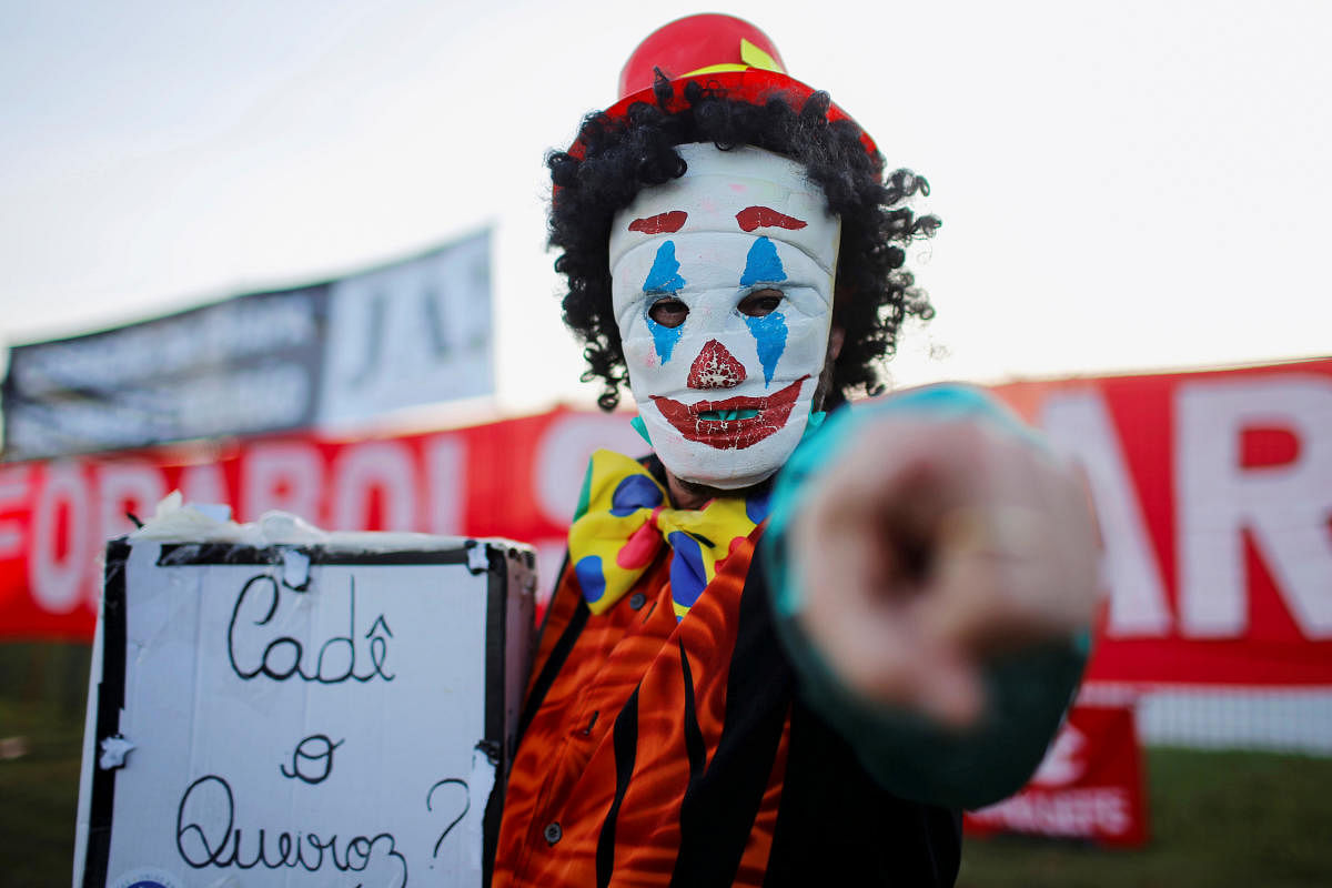 A demonstrator wearing a clown mask and holding a sign that says