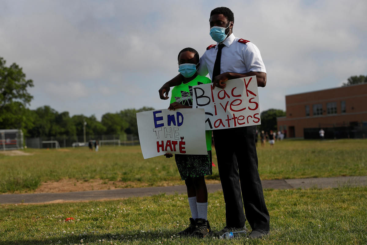 A man puts his arm on the shoulder of a child holding signs during a protest against racial inequality in the aftermath of the death in Minneapolis police custody of George Floyd, in Malverne, New York, U.S. Credit/Reuters Photo