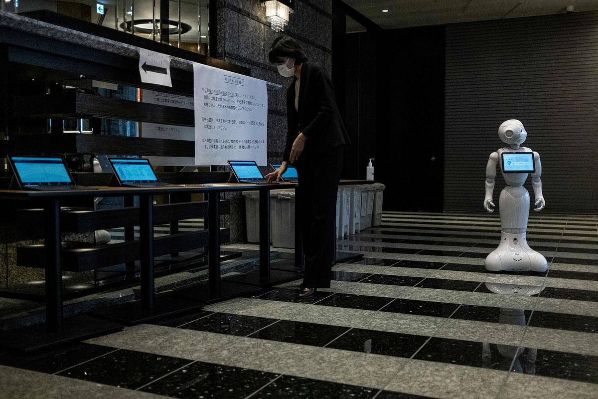 An official (L) wearing a face mask checks a computer as a greeting robot named
