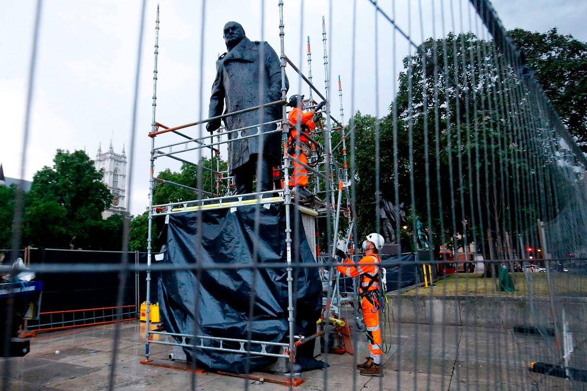 Workers remove the boards protecting the statue of former Prime Minister Winston Churchill from vandalism during anti-rascism portests. Credit: AFP Photo