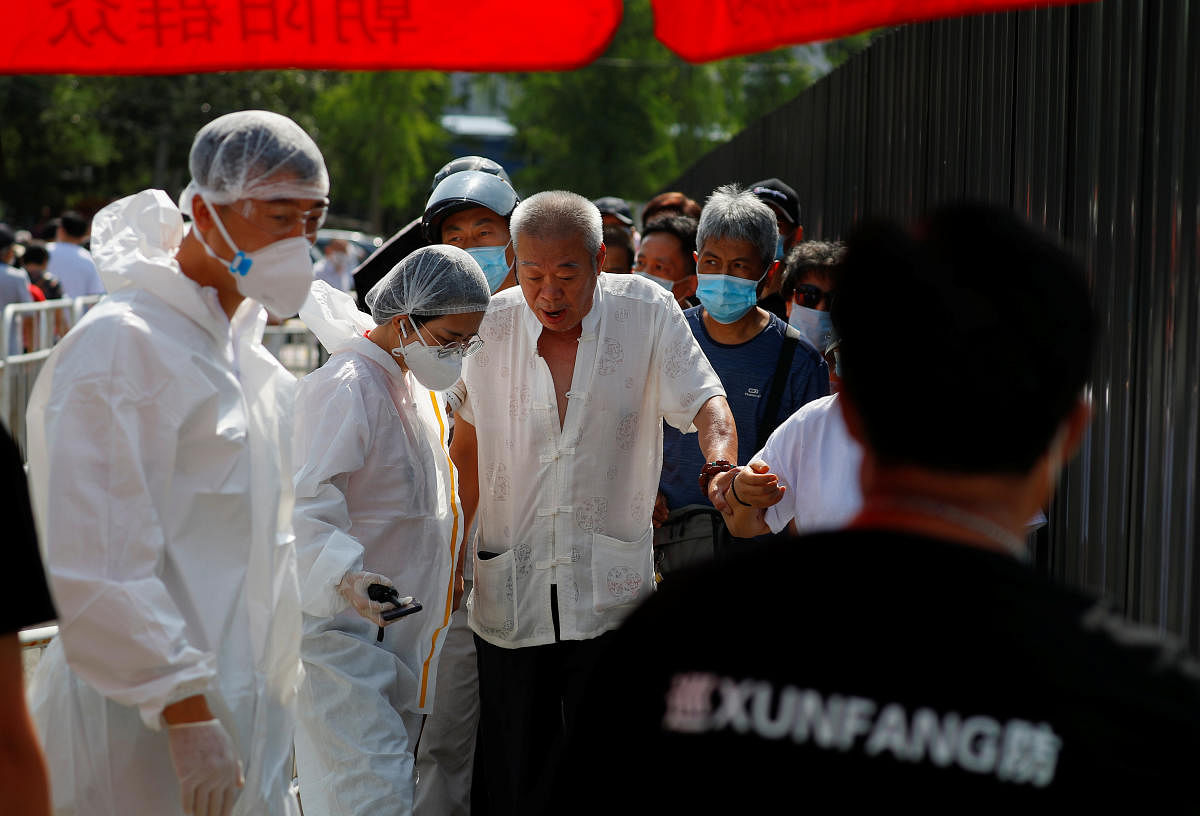 Members of the medical team dressed in PPE are seen as people line up to receive nucleic acid tests at a temporary testing site after a new outbreak of Covid-19 in Beijing. Reuters