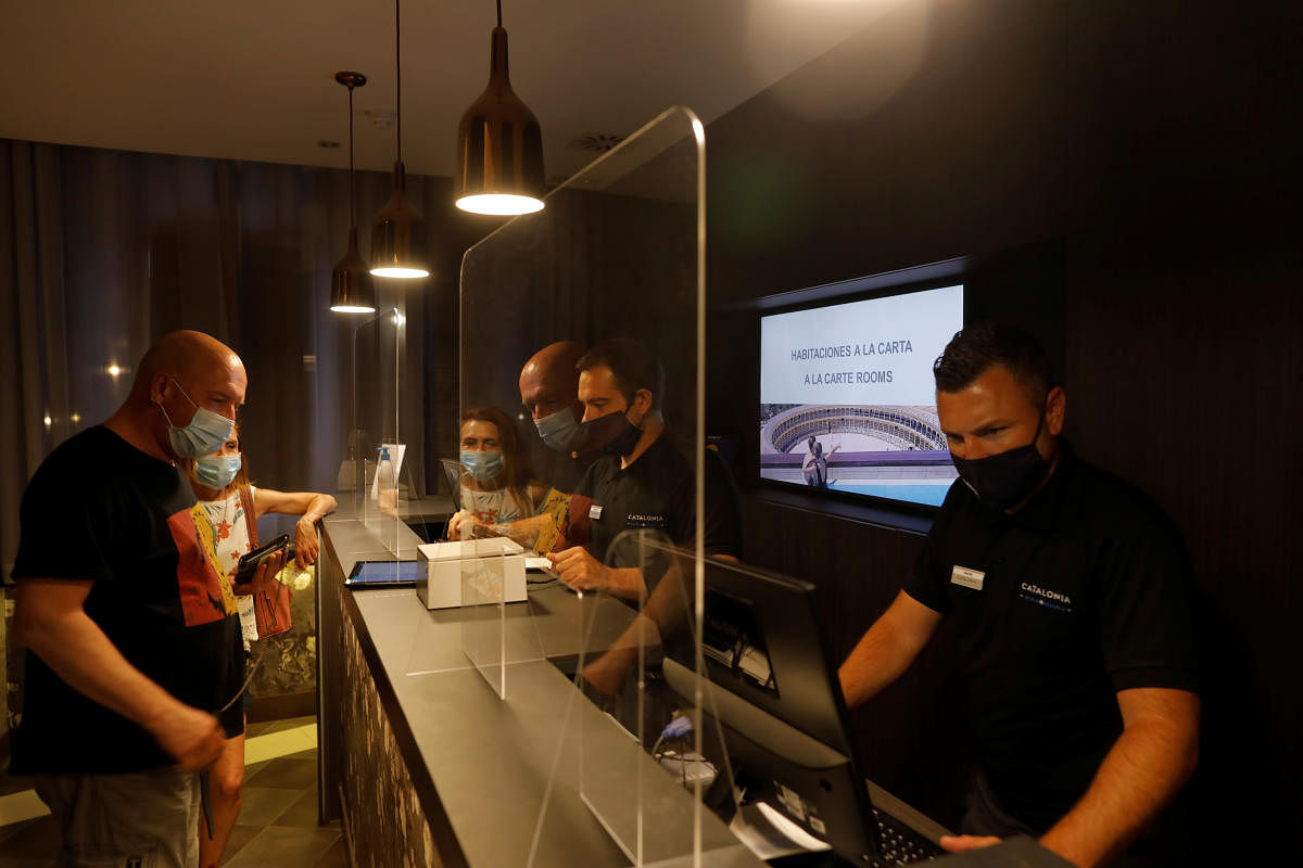 German tourists are attended by receptionists, , wearing protective face masks and with safety measures to prevent the spread of Covid-19, as they do the check-in at the reception desk at Catalonia Ronda hotel, in Ronda. Reuters
