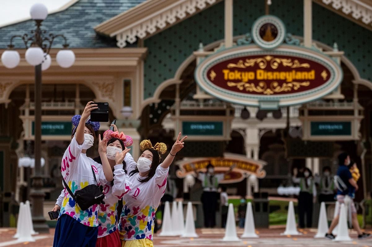 Visitors wearing face masks pose for a selfie at the entrance of Tokyo Disneyland during the reopening day of the park in Urayasu, near Tokyo on July 1, 2020. Credit/AFP Photo