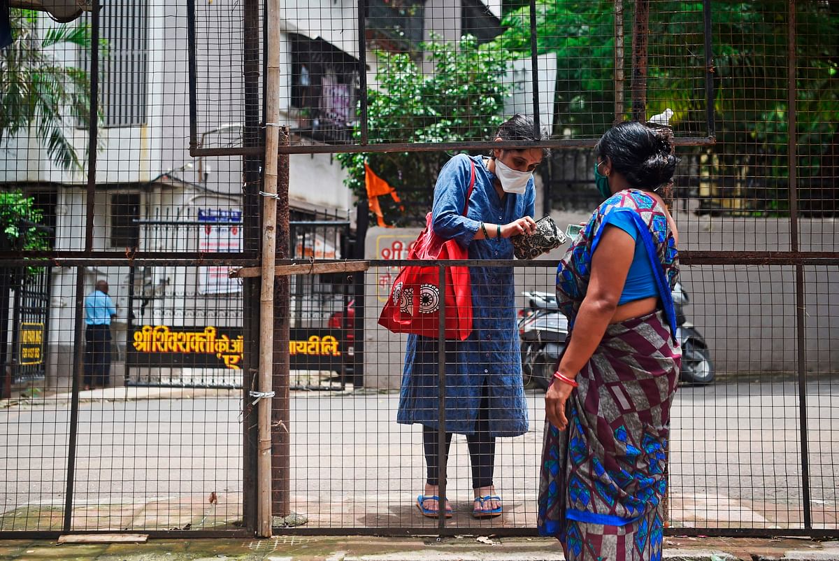 A woman (L) wearing a facemask purchases vegetables from behind the closed entrance of a residential society, due to the COVID-19. Credits: AFP Photo