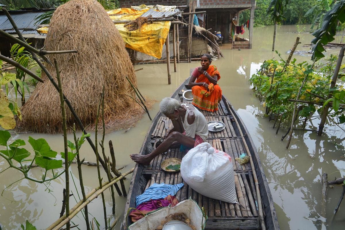 Flood affected villagers sit on a boat in front of their partially submerged house, at Chandrapur in Kamrup district. Credits: PTI