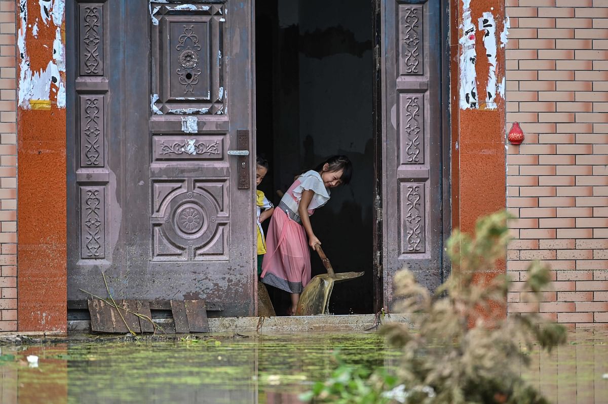 Children remove water from inside their house in Longkou village due to torrential rains in Poyang county, Shangrao city in China's central Jiangxi province on July 16, 2020. - The vast Yangtze drainage area has been lashed by torrential rains since last month, leaving 141 people dead or missing and forcing the evacuation of millions more across several provinces. Credit: AFP