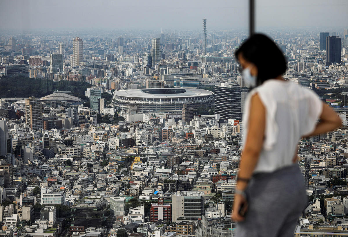 The National Stadium, the main stadium of Tokyo 2020 Olympics and Paralympics, is seen past a visitor wearing a protective face mask amid the coronavirus disease (COVID-19) at an observation deck in Tokyo, Japan July 20, 2020. Credit: REUTERS