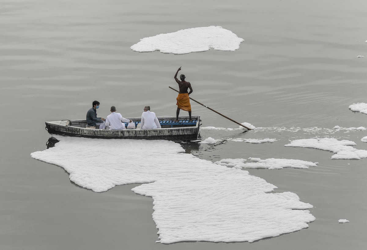 A family throws some religious waste into the Yamuna River as toxic foam floats on its surface owing to pollution, at Kalindi Kunj in New Delhi amid lockdown. Credit: PTI