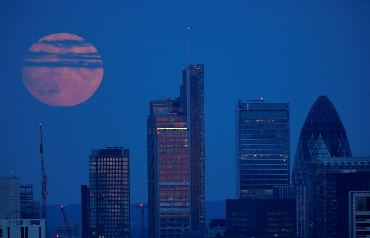 The full moon is seen rising over the City of London financial district in London, Britain, August 2, 2020. Credit: REUTERS