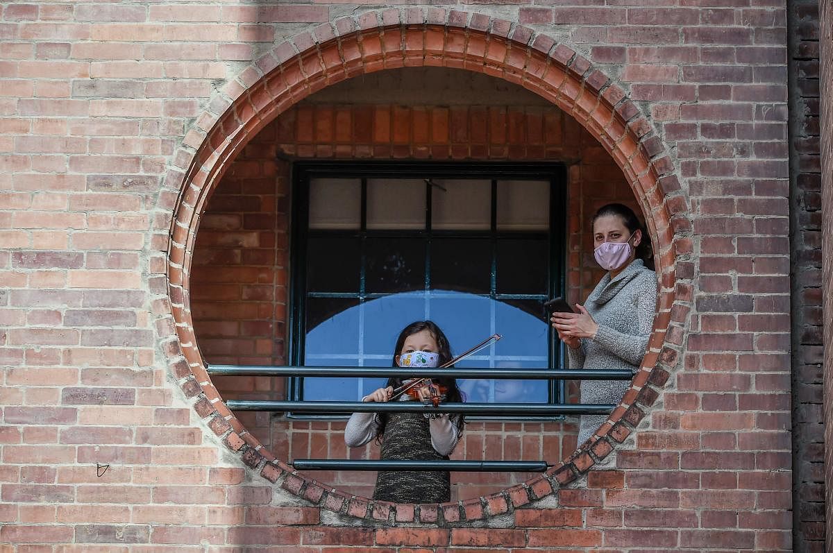 A girl wearing a face mask plays a violin from a balcony of her house during the 482th anniversary of the city of Bogota. Credit: AFP