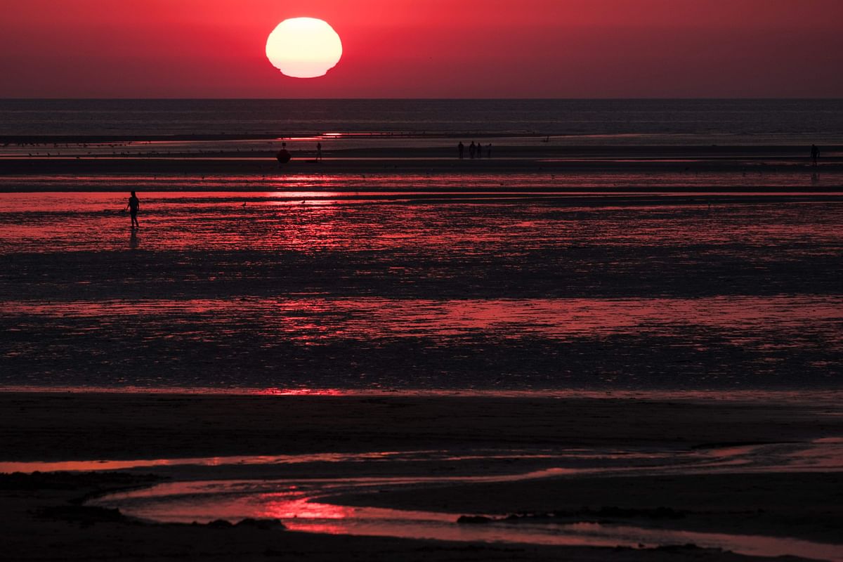 People walk on a beach at sunset in Houlgate, northern France, on August 8, 2020. Credit: AFP