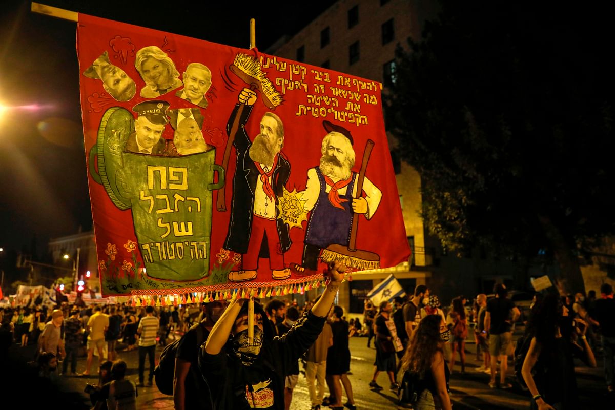 A protester holds a banner during a demonstration against the Israeli government near the Prime Minister's residence in Jerusalem on August 8, 2020. Credit: AFP