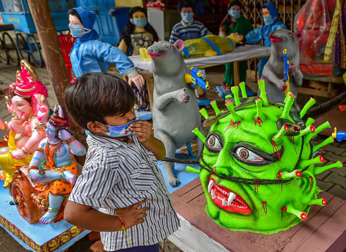 A boy stands near a coronavirus themed idol for Puja festivities at a workshop, in Bengaluru. Credit: PTI
