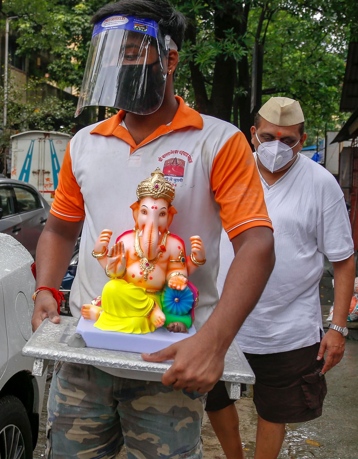 A devotee, wearing face shield amid COVID-19 pandemic, carries an idol of Lord Ganesha to install at his for Ganesh Utsav, in Thane. Credit: PTI