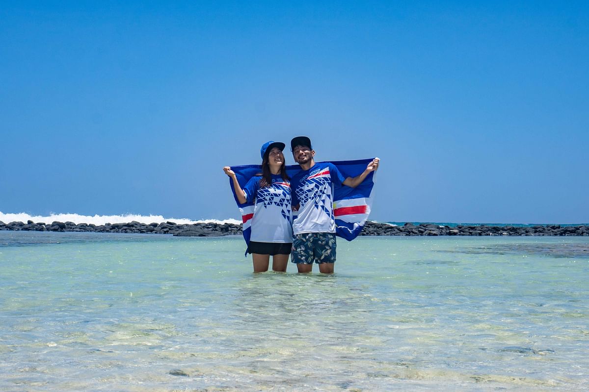 This handout picture taken on August 15, 2020 and provided by instagram@rikiya_trip on August 24 shows Japanese couple Rikiya (R) and Ayumi Kataoka (L) posing with the official Olympic Cape Verde uniform and national flag as a gift from the National Olympic Committee in Santa Maria. Credit: AFP Photo