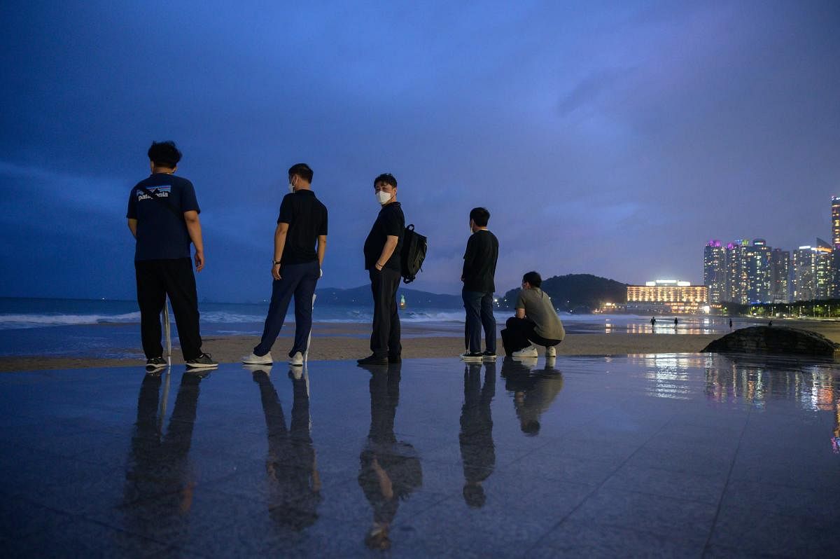 People stand on a promenade deck as they watch the waves during heavy swells brought by the approaching typhoon Maysak on Haeundae beach in Busan on September 2, 2020. Flights were grounded in South Korea and storm warnings issued on both sides of the Korean peninsula as a typhoon forecast to be one of the most powerful in years made its approach. Credit: AFP Photo