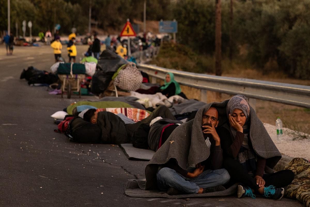 A couple sits covered with a blanket as refugees and migrants camp on a road following a fire at the Moria camp on the island of Lesbos, Greece. Credit: Reuters Photo