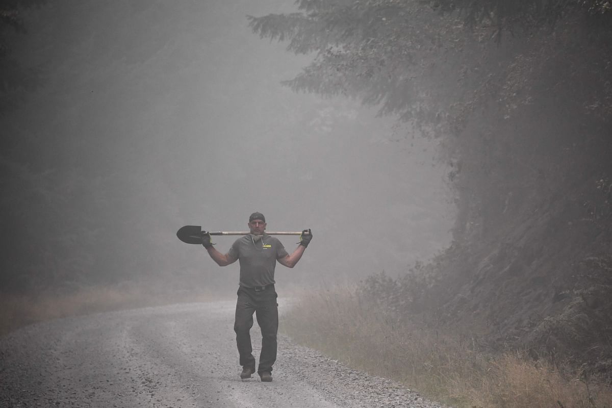 A local resident helping to put out hotspots and cut fire roads walks down a smoky road with a shovel over his shoulders, in Molalla, Oregon. A large number of volunteers gathered to help prevent fire from advancing into the town of Molalla. Of the at least 33 people killed by the blazes since the beginning of summer, 25 died this week alone. Credit: AFP