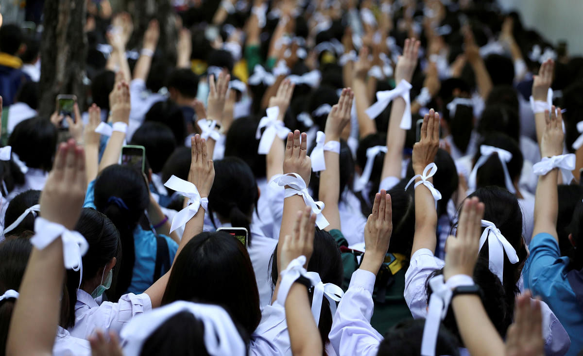 Students wearing white ribbons on their hair and wrists make the three-finger salute to show support for the student-led democracy movement outside the Education Ministry in Bangkok, Thailand. Credit: Reuters Photo