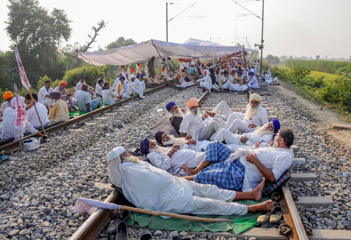 Farmers block a railway track during their protest against the new farm bills, at Devi Dass Pura village, about 20 kilometers from Amritsar. Farmers across the state have threatened to stop train services to press for the rollback of three new farm bills of the Central government, claimed to be against the interest of farmers. Credit: PTI Photo