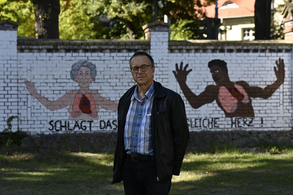 Martin Osinski poses for a picture in a public garden with graffiti on the background wall reading