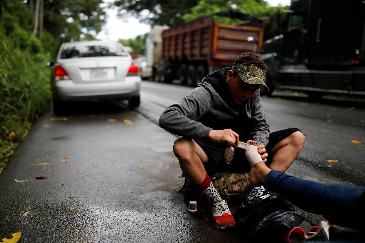 A Honduran migrant trying to reach the US treats the foot of a fellow migrant on the side of the road after bursting through a border checkpoint to enter Guatemala illegally, in Izabal, Guatemala. Credit: Reuters Photo