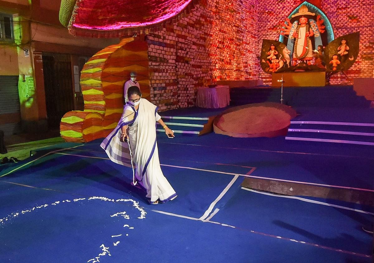 West Bengal Chief Minister Mamata Banerjee showing organizers how to make round marks for the visitors, to maintain social distancing norms, after inaugurating a community Durga Puja pandal, in Kolkata. Credit: PTI Photo