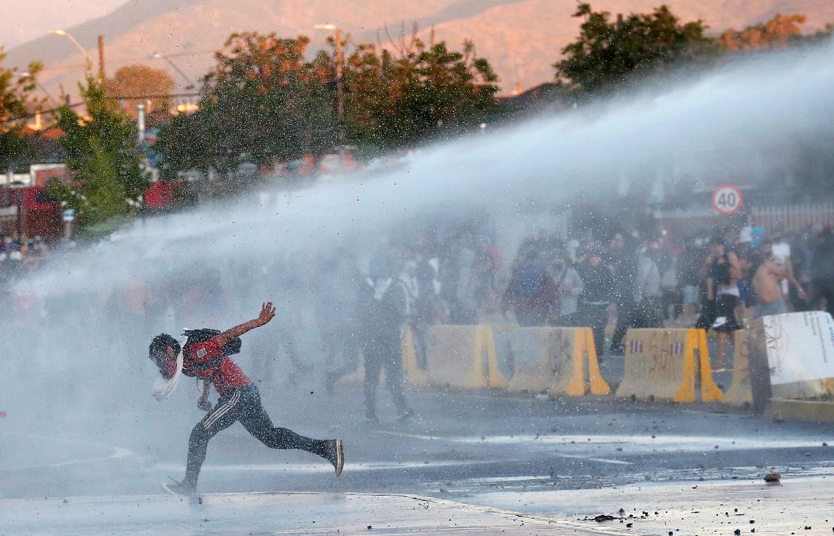 A demonstrator is sprayed by riot police water cannon during a protest against Chile's government, on the one-year-anniversary of the protests and riots in 2019, in Quilpue, Chile. Credit: Reuters.