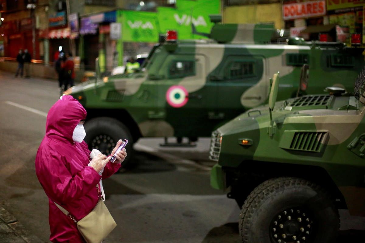 A woman wears a protective mask as she stands next to army armored vehicles during the presidential election in La Paz, Bolivia. Credit: Reuters.