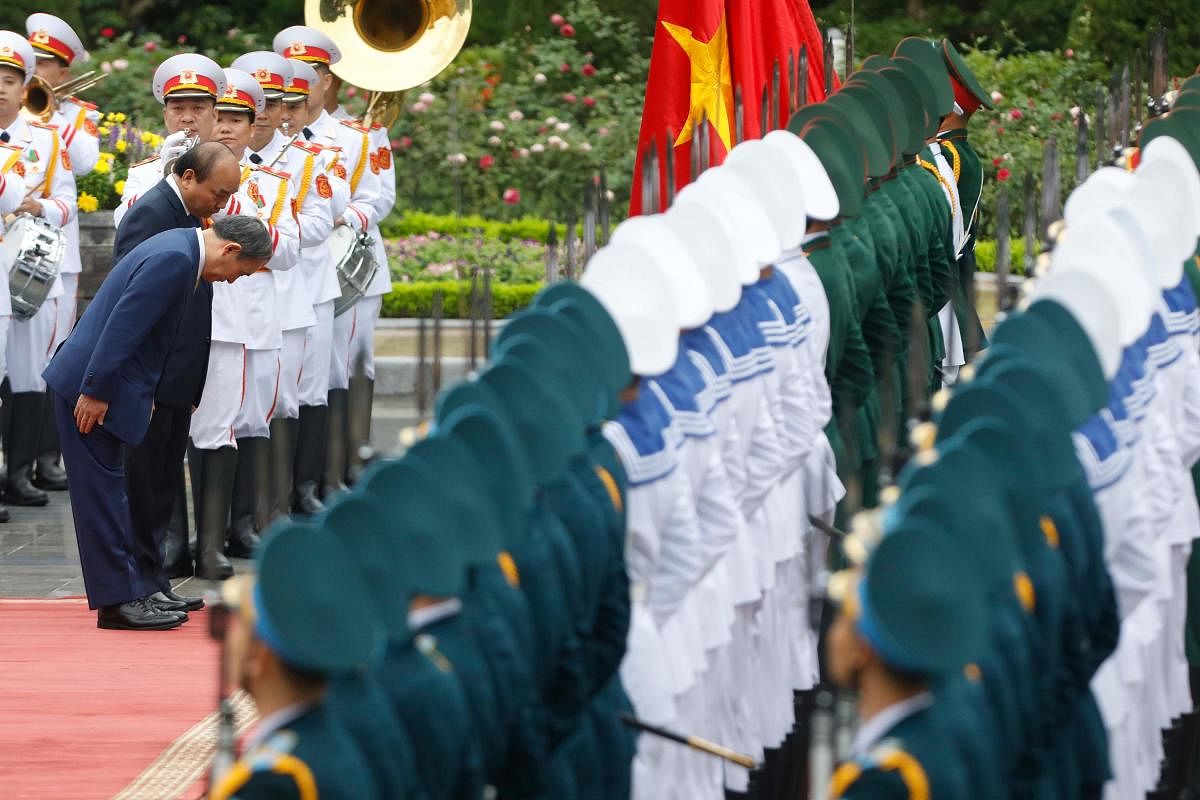 Japan's Prime Minister Yoshihide Suga (L front) and Vietnam's Prime Minister Nguyen Xuan Phuc (L back) bow as they review an honour guard during an official visit at the Presidential Palace in Hanoi. Credit: AFP.